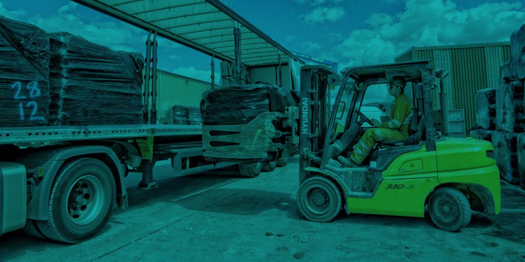 Countrystyle image of fork truck loading bails onto truck.
